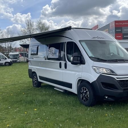 Ein grau-weißer Wohnwagen mit einer verlängerten Markise steht auf grünem Gras