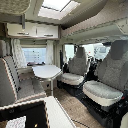 Innenraum eines modernen Wohnmobils mit Esstisch, zwei Fahrersitzen und großzügigem Stauraum mit Oberlicht.