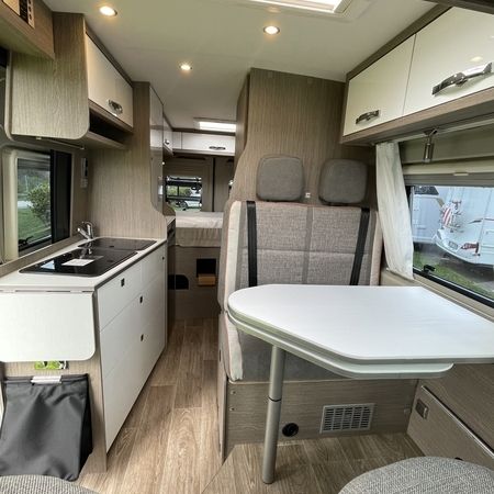 Innenansicht eines modernen Wohnmobils mit Küchenzeile, Essbereich mit Tisch und bequemen Sitzgelegenheiten