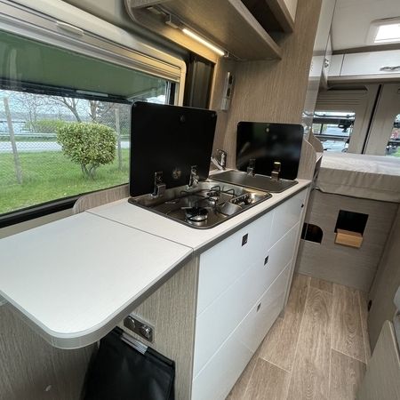 Kompakte Wohnmobilküche mit Zwei-Flammen-Herd, Arbeitsfläche, Schubladen und großem Seitenfenster