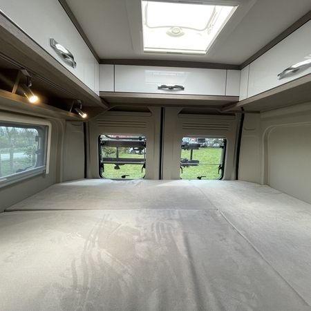 Innenraum eines Wohnmobils mit einem gemütlichen Schlafbereich mit weicher, heller Bettwäsche, Stauschränken und Fenstern