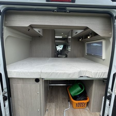 Innenraum eines Wohnmobils mit geöffneten Hintertüren, mit Doppelbett und Stauraum