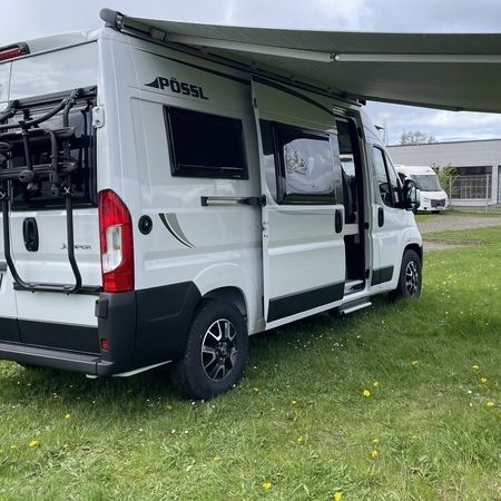 Ein grau-weißer Wohnwagen mit einer verlängerten Markise steht auf grünem Gras