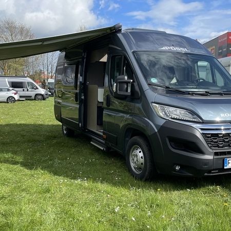 En autocamper, der er parkeret på en eng ved siden af et farvestrålende telt under en strålende blå himmel.