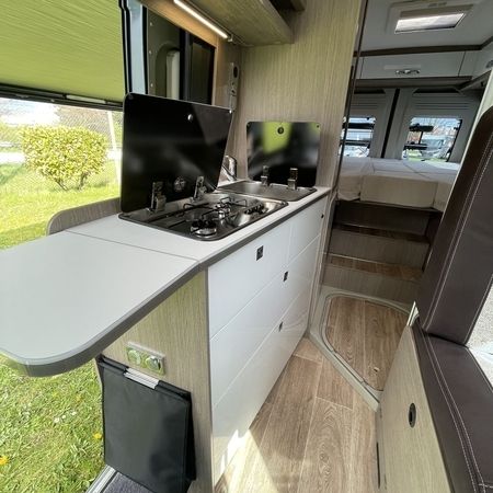 Indvendigt i en autocamper med kompakt køkken og hyggelig seng