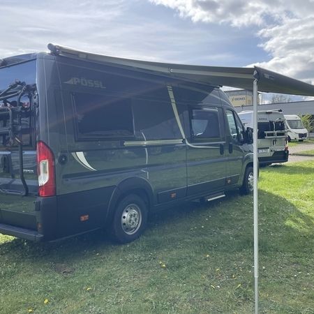 En autocamper, der er parkeret på en græsplæne og har et soltag.