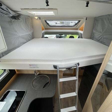 Indvendigt i en autocamper med en hyggelig seng og et kompakt håndvask