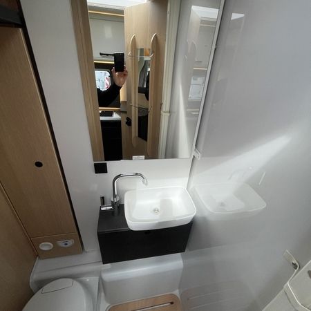 Et badeværelse med håndvask, toilet og et spejl på væggen