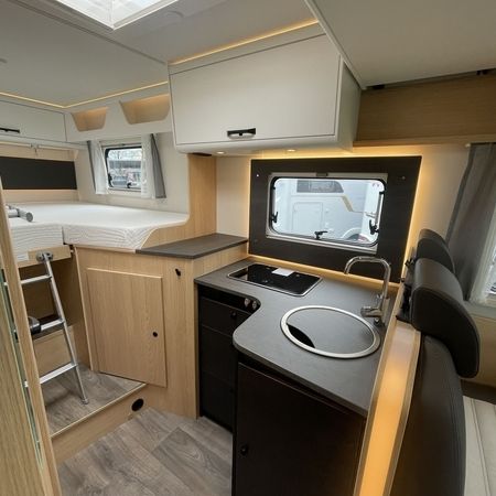 Interiør i et lille autocamper med vask og komfur, der tilbyder et kompakt opholdsrum og et funktionelt design.