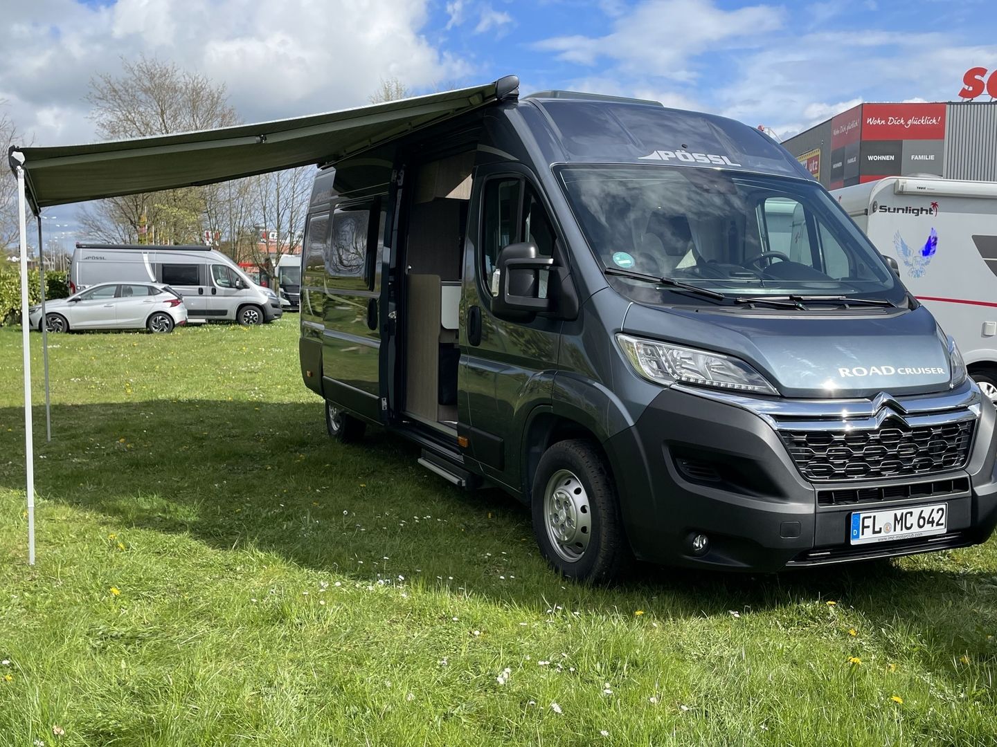 En autocamper, der er parkeret på en eng ved siden af et farvestrålende telt under en strålende blå himmel.